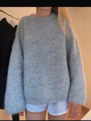 Ljusgrå oversized stickad tröja - Mysig ljusgrå stickad tröja med oversized passform och rund hals. Tröjan har långa, vida ärmar och är tillverkad i mohair/woolblendmaterial som ger en avslappnad look. Perfekt för lager på lager och chill dagar.