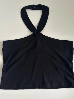 Svart halterneck tubtopp från Vero Moda - Trendig svart tubtopp från Vero Moda med bred halterneck och knappstängning i nacken. Toppen är ärmlös och har en clean, croppad passform som passar perfekt till höga jeans eller kjol. Tillverkad i mjukt material för en bekväm känsla. Helt NYTT. 