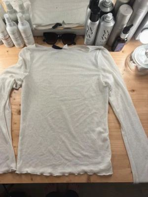 Vit ribbad långärmad topp - Vit långärmad tröja blus/topp i ett lite genomskinligt ribbat tyg från Hm, biland aktig kant nedtill, i storlek S