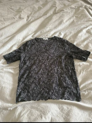 Grå spetsblus med halvärm - Säljer en grå blus i spets med vackert broderat mönster. Blusen har rund halsringning och halvärm, samt fina vågiga kanter nedtill och vid ärmsluten. Perfekt för dig som gillar detaljer och en romantisk look.storlek s