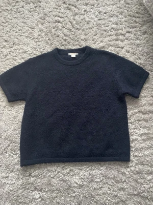 Mörkblå stickad t-shirt Gina Tricot - Mörkblå stickad t-shirt från Gina Tricot med korta ärmar och rund halsringning. Tröjan är enkel att matcha till vardag. Använd fåtal gånger. Pris kan diskuteras.