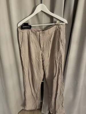 Beige linnebyxor från lager 157 - Säljer ett par ljusbeige linnebyxor med raka ben. Byxorna har knapp och dragkedja framtill samt sidofickor.