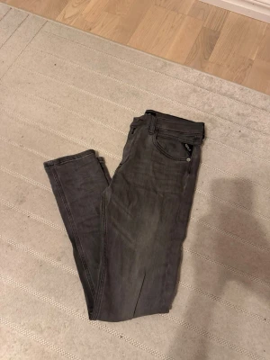 Gråa slim fit jeans från replay  - Snygga grå slim fit jeans med klassisk femficksdesign och dragkedja. Jeansen har en smal passform och är tillverkade i ett mjukt denimtyg som ger en skön känsla. Perfekta för dig som gillar en stilren och enkel look.