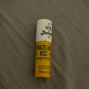 Sol de Janeiro Brazilian Kiss läppbalsam - Fuktgivande läppbalsam från Sol de Janeiro i modellen Brazilian Kiss. Hylsan är gul och vit med svart text och har en rundad form. Innehåller cupuaçusmör som ger näring och mjukgör läpparna. Perfekt att ha i väskan för återfuktade läppar hela dagen.