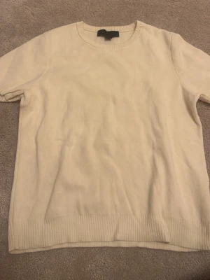 Créme färgad fin tshirt  - En enkel och stilren beige stickad t-shirt med korta ärmar och rund halsringning. Tröjan har ribbade muddar vid ärmslut och nederkant för en clean look. Perfekt att matcha med jeans eller kjol för en avslappnad vibe.