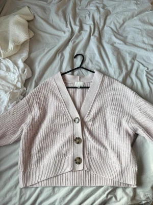 Ljusrosa ribbad kofta med stora knappar - Ljusrosa ribbad kofta med knappar framtill,v-ringning och breda muddar.