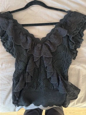 Svart spetsblus med volang - Säljer en svart blus i spets med stora volangdetaljer runt halsringningen.