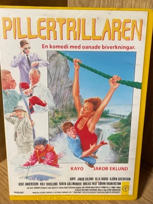 Pillertrillaren VHS - Svensk komedibok med titeln 'Pillertrillaren'. Omslaget är färgglatt med illustrationer av karaktärer i vildmarksäventyr. Utgiven av Svensk Filmindustri 1993.