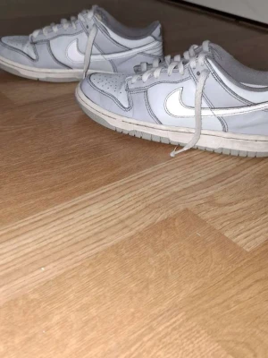 Nike vita låga sneakers - Säljer ett par klassiska vita Nike sneakers med lågt skaft och den ikoniska swoosh-loggan på sidan. Skorna har vita snören, gummisula och är tillverkade i läder och textil. Perfekta för en clean och stilren look.