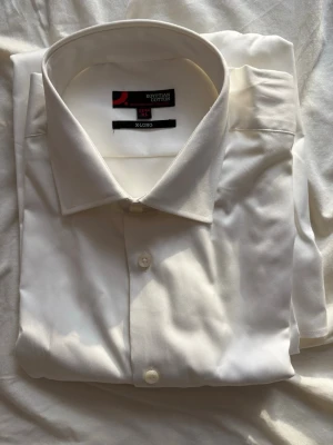 Vit skjorta i egyptisk bomull XL - Klassisk vit skjorta från Dressmann i lyxig egyptisk bomull. Skjortan har lång ärm, knappar framtill och en stilren krage. Perfekt för dig som gillar en clean och tidlös look. Modellen är X-Long för extra längd.