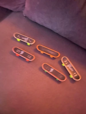 Fem fingerboards med färgglada hjul - Säljer ett set med fem fingerboards i svart och träfärg med olika färgglada hjul i grönt och orange. Perfekta för tricks och samling! Några har tryck på ovansidan och alla har klassisk skateboardform.