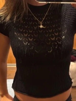 Svart zara topp - Svart stickad topp med korta ärmar och en kortare passform. Toppen har ett snyggt hålmönster framtill som ger en trendig look. Perfekt att styla med jeans för en vardaglig look💞(lånade bilder)