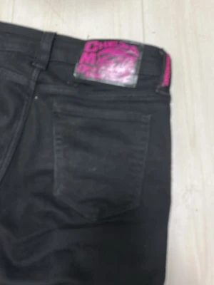 Svarta jeans från Cheap Monday - Säljer ett par svarta jeans från Cheap Monday med klassisk femficksmodell och en cool rosa logga på bakfickan. Jeansen har rak passform och är tillverkade i ett mjukt bomullsmaterial med lite stretch för extra komfort. De är i storlek 26/30 och om ni inte är nöjda med priset diskuterar vi 