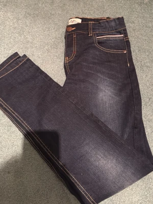 Mörkblå jeans med kontrastsömmar - Snygga mörkblå jeans från Hampton repupublic. Pyret med klassisk femficksdesign och tydliga kontrastsömmar i orange. Jeansen har en rak passform och är tillverkade i slitstarkt denimtyg. Perfekta för en trendig och avslappnad look. 158 passar de för och är sjukt bra för priset! 