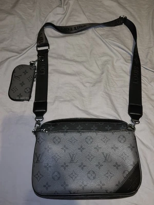 Louis Vuitton grå axelväska monogram - Snygg axelväska från Louis Vuitton i grått och svart med klassiskt monogrammönster. Väskan har bred justerbar axelrem med logga, samt två mindre avtagbara väskor. Tillverkad i slitstarkt läder med silverfärgade detaljer. Perfekt för dig som vill ha en trendig och praktisk väska. Pris kan alltid diskutera 