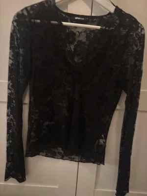 Svart spetsblus från Gina Tricot - Snygg svart långärmad spetsblus från Gina Tricot med blommigt mönster. Blusen har v-ringning och är genomskinlig, perfekt att styla med ett linne under. Passformen är normal och materialet känns lätt och luftigt.