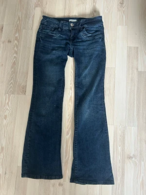 Mörkblå bootcut jeans - Säljer ett par mörkblå bootcut jeans med klassisk femficksdesign och snygga slitningar. Jeansen har normal midja, bälteshällor och är tillverkade i stretchig denim för skön passform. Perfekta för dig som gillar retrovibbar och vill ha ett par jeans med lite vidare ben. Storlek 158 men passar mig som har xs/s
