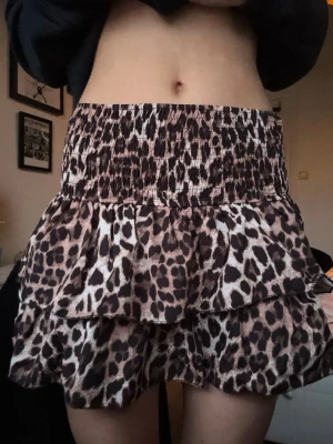 Leopardmönstrad volangkjol - Kort kjol med leopardmönster och dubbla volanger. Kjolen har bred, smockad midja för en bekväm passform och är perfekt för dig som vill sticka ut. Materialet känns lätt och flowy.