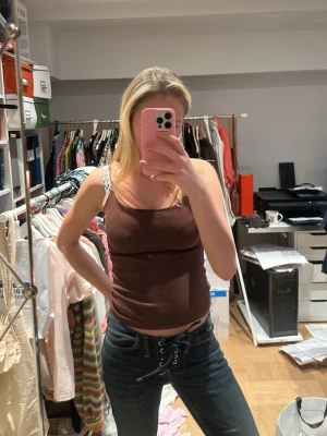 Brun croppad linnetopp - Säljer en brun croppad linnetopp med smala axelband. Toppen har en enkel och stilren design som passar perfekt till jeans eller kjol. Materialet känns mjukt och bekvämt mot huden.