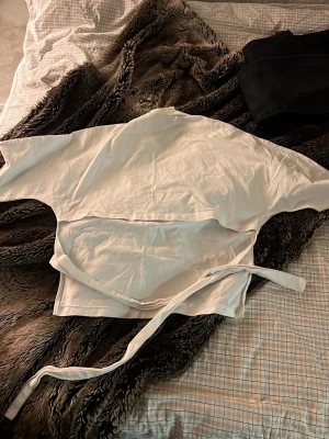 Vit omlottopp med knytband - Snygg vit omlottopp med långa ärmar och knytband i midjan. Perfekt för en stilren och trendig look. Toppens material känns mjukt och lätt, vilket gör den bekväm att bära hela dagen. Kom privat för fler bilder på❤️