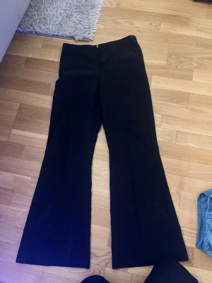 Svarta utsvängda kostymbyxor Gina Tricot - Säljer ett par svarta kostymbyxor från Gina Tricot med utsvängda ben och hög midja. Byxorna har dragkedja i sidan och är perfekta för en trendig och stilren look. Materialet är mjukt och följsamt, vilket gör dem bekväma att bära hela dagen.