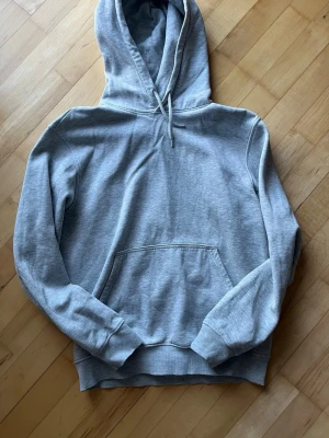 Grå hoodie från Weekday - Säljer en klassisk grå hoodie från Weekday i storlek S. Hoodien har en stor huva med dragsko, magficka och ribbade muddar vid ärmar och nederkant. Tillverkad i mjuk bomullsblandning som är superbekväm och perfekt för chill dagar.
