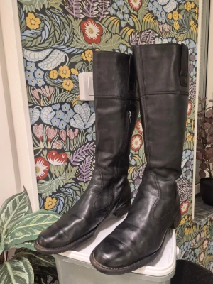 Svarta knähöga läderstövlar från Ecco 41 - Säljer ett par klassiska svarta knähöga stövlar i äkta läder. De har dragkedja på insidan och en stilren, tidlös design med rundad tå och låg klack. Perfekta till jeans eller kjol för en snygg och enkel look.