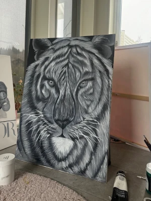 Svartvit tigermålning på canvas - Unik handmålad tavla föreställande ett tigeransikte i svart, vitt och grått. Målningen är gjord på canvas och har starka kontraster och detaljerade penseldrag som ger ett intensivt uttryck. Perfekt som cool inredningsdetalj för att lyfta vilket rum som helst.