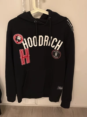 Hoodrich limited edition helt ny använd 3 gånger  - Svart hoodie från Hoodrich med stora vita bokstäver på bröstet och flera broderade patches i rött, vitt och svart. Klassisk känguruficka framtill, dragsko i huvan och ribbade muddar. Perfekt för en streetwear-look.