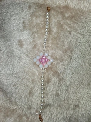 Pärlarmband med rosa och vita pärlor - Snyggt armband med vita pärlor och ett mittparti av rosa och vita pärlor i diamantform. Armbandet har en klassisk och söt design med glansiga pärlor som ger en fräsch look. Perfekt accessoar för att lyfta din outfit med lite extra färg och stil.