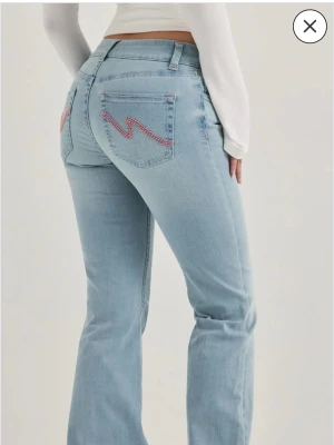 Nelly jeans- Low waist  - Säljer ett par ljusblå lågmidjade bootcut jeans med rosa zigzag-broderi på bakfickorna. Jag har använt jeansen 3 gånger men dom är lite för korta så därför säljer jag dom😊Skriv till mig om du vill se egna bilder! 