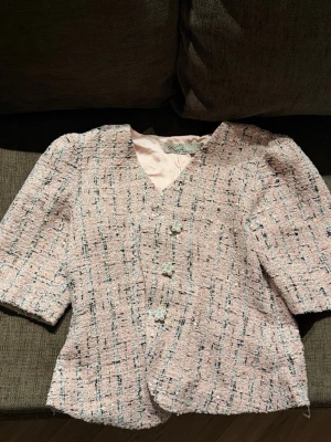 Rosa topp med pärlknappar - Snygg rosa tweedkavaj från Koton med trekvartsärmar och pärlknappar framtill. Kavajen har ett klassiskt rutmönster i svart och vitt samt ljusrosa foder. Perfekt för en chic och trendig look.