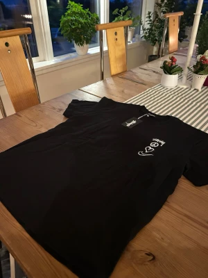 Svart Stüssy t-shirt med tryck - Säljer en svart t-shirt från Stüssy med vitt tryck på bröstet som visar ett peace-märke, hjärta och swoosh. Klassisk passform och rund hals. Perfekt för dig som gillar streetwear och vill ha något stilrent men ändå med edge.