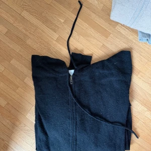 Svart cashmere hoodie med dragkedja från Davida - Säljer en svart hoodie från Davaid i storlek L. Hoodien har dragkedja framtill, justerbar huva med snören och är tillverkad i ett mjukt tyg som känns skönt mot huden. Perfekt för en avslappnad och stilren look.