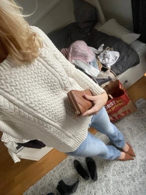 Vit kabelstickad tröja med polokrage - Snygg vit kabelstickad tröja med polokrage och grovt mönster. Tröjan har en avslappnad passform och långa ärmar, perfekt för lager-på-lager. Materialet ser ut att vara mjukt och värmande, passar till jeans eller kjol.