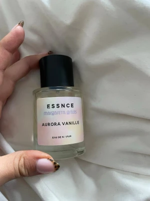 Aurora Vanille parfym från Essnce - Aurora Vanille från Essnce x Margareta Grääs är en Eau de Parfum i en rund, genomskinlig glasflaska med svart lock. Doften har en söt och mjuk vaniljkaraktär. Flaskan har en stilren etikett i ljusa pastellfärger.