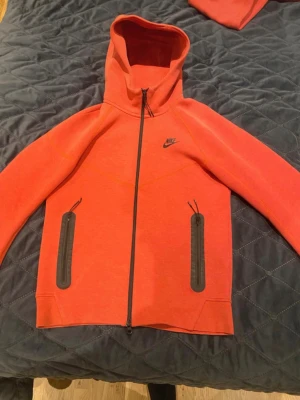 Röd Nike zip hoodie med huva - Snygg röd tracksuit från Nike med svart logga på bröstet. Tröjan har hel dragkedja, två svarta dragkedjeförsedda fickor framtill och en skön huva. Perfekt för en sportig och avslappnad stil. Den är i riktigt gott skick, båda byxor och tröjan k storlek S men den sitter (passar storlek M) 