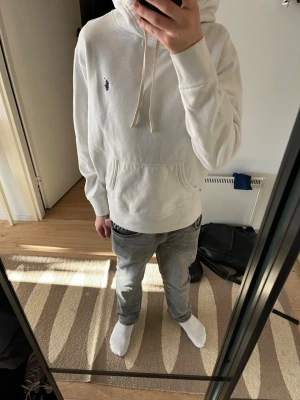 Vit hoodie från Polo Ralph Lauren - Säljer en clean vit hoodie från Polo Ralph Lauren med den klassiska lilla marinblå loggan på bröstet. Hoodien har huva med dragsko och en stor magficka. Tillverkad i mjukt bomullsmaterial, perfekt för chill dagar eller när du vill ha en enkel men snygg look.
