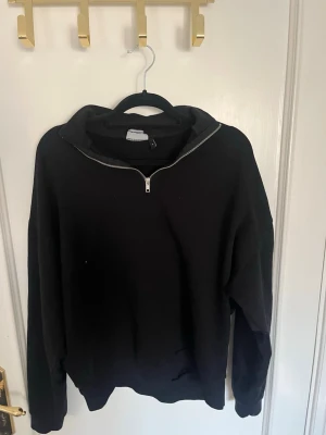 Svart halvzip hoodie från ASOS DESIGN - Svart hoodie från ASOS DESIGN med halv dragkedja framtill och hög krage. Tillverkad i mjukt material, perfekt för en avslappnad stil. Klassisk passform med ribbade muddar vid ärmslut och nederkant.