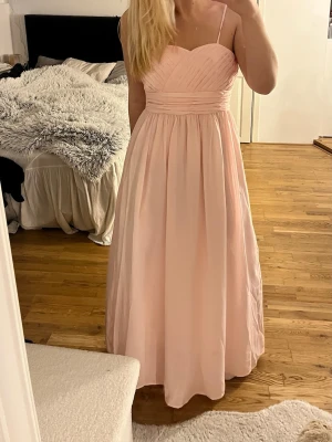 Rosa balklänning  - En superfin rosa balklänning. Den funkar både med och utan band ifall man skulle vilja ta av dom. Storlek S. Midjemått: 77cm. Bystmått: 82cm. Längd:126 cm. Dragkedjans längd: 43cm💕 klänningen är för liten för mig därav att dragkedjan inte är uppdragen helt.