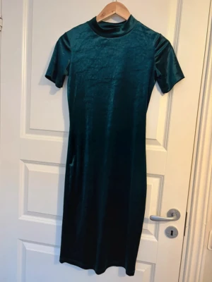 Mörkgrön sammetsklänning - Figursydd mörkgrön klänning i mjuk sammet med korta ärmar och rund hals. Klänningen har en rak passform och slutar strax under knät, perfekt för dig som gillar en stilren look med lite lyxig känsla. Kolla min profil för fler plagg! 🥰
