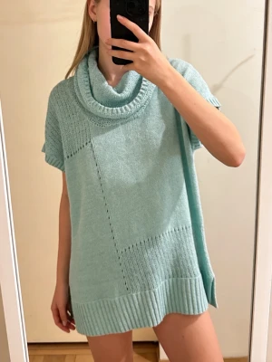 Ljusblå stickad polotröja Bonita - Snygg ljusblå stickad polotröja från Bonita med korta ärmar och bred ribbad kant nedtill. Tröjan har en stor, mysig polokrage och ett coolt patchwork-stickat mönster. Perfekt för lager-på-lager under hösten och vintern.