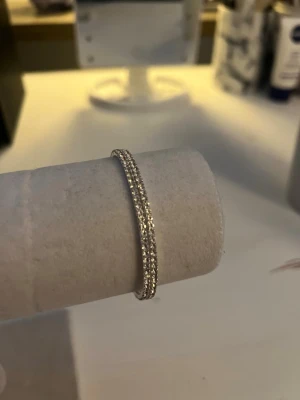 Glittrigt silverfärgat armband - Snyggt armband i silverfärg med gnistrande små pärlor runt hela bandet. Armbandet har en rund form och är elastiskt vilket gör det enkelt att ta på och av. Perfekt för dig som gillar stilrena och glittriga accessoarer. Orginal pris 200kr. (Använt 1 gång)