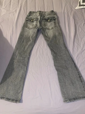 Grå bootcut jeans med fickdetaljer - Säljer ett par grå bootcut jeans med snygga fickdetaljer bak och klassisk femficksdesign. Jeansen har en lätt tvättad look och vida ben. Perfekta för dig som gillar en avslappnad men trendig stil.