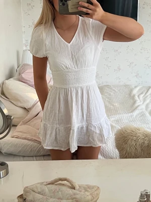 Studentklänning Gina Tricot - Supersöt vit klänning med v-ringning, smock i midjan och volangkant nedtill. Skulle passa perfekt som studentklänning! Jag har bara använt den en gång för jag har andra klänningar jag gillar, den är storlek 134-146 men passar mig fint som har xs-s vanligtvis🫶