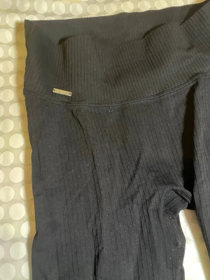 Svarta ribbade leggings från Aim'n - Säljer ett par svarta ribbade träningsbyxor från Aim'n med hög midja och stretchigt material. De har en diskret logga framtill och sitter tight längs benen. Perfekta för en sportig och bekväm look. Lappen är bortklippt men om jag minns rätt är det strl M.