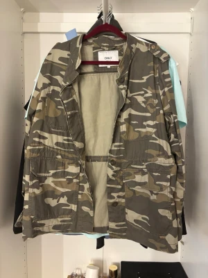 Camo militärjacka från ONLY - Säljer en camouflagefärgad militärjacka från ONLY med flera stora fickor framtill och knappdetaljer på axlarna. 