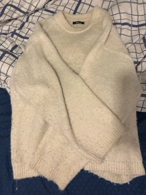 Oversized beige stickad tröja - Mysig oversized stickad tröja i beige med rund hals och långa ärmar. Tröjan har en enkel, rak passform och ribbstickade muddar vid ärmslut och nederkant. Perfekt för lager på lager och chill dagar.