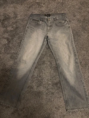 Grå raka jeans från Earthquake - Snygga grå jeans från Earthquake med raka ben och coola detaljer som dragkedjor på bakfickorna. Klassisk femficksmodell i slitstark denim, perfekt för dig som gillar en avslappnad men trendig look.