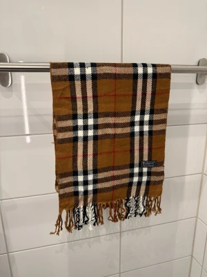 Burberrys Halsduk/Scarf Brun - Burberrys Halsduk / Scarf  Färg: Brun Material: 100% Lammull Unisex  Fint skick!